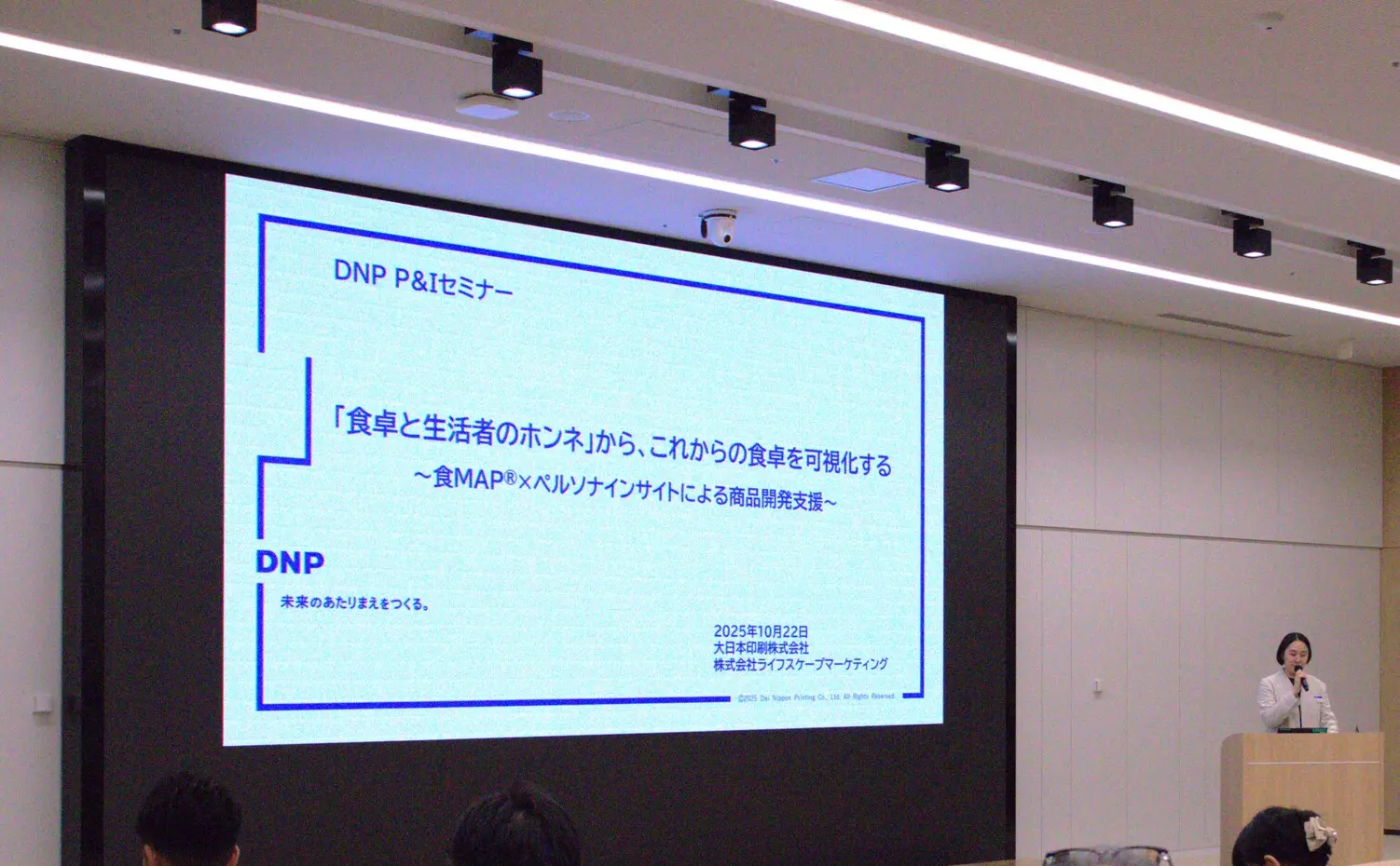 DNP P&Iセミナーの登壇風景—スクリーンにタイトルスライド、参加者を前に講演する様子