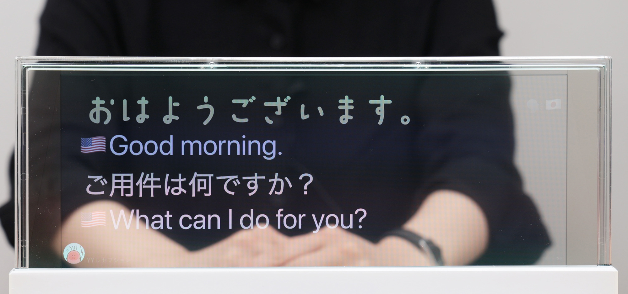 DNP対話支援システムの画面。透明な液晶ディスプレイに話した内容が表示され、日本語が英語に翻訳されている。