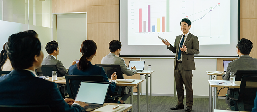 棒グラフと折れ線グラフを映した会議室で、講師が参加者に説明する様子