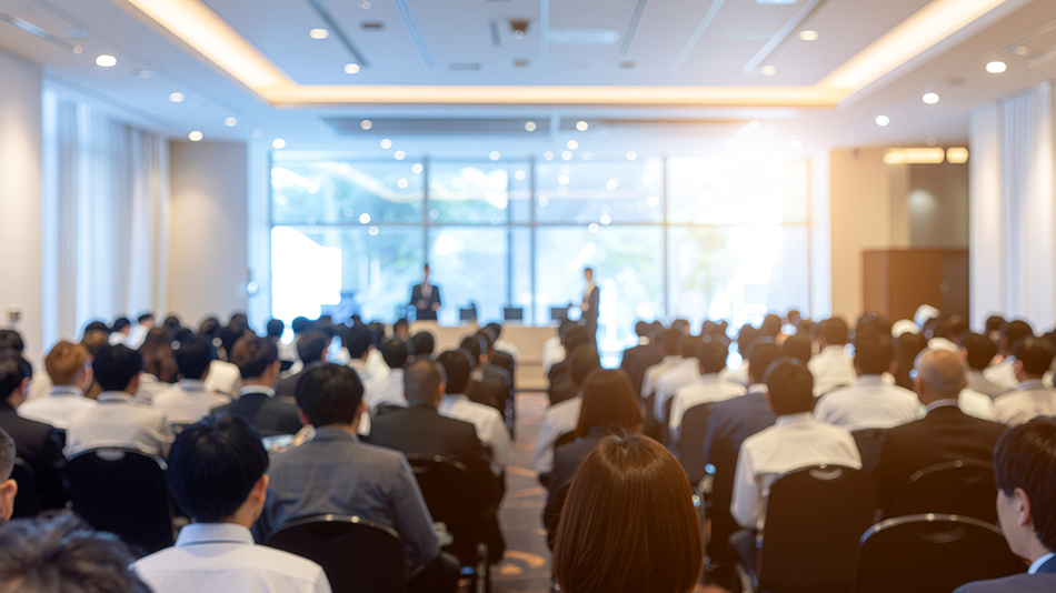 広い会場で登壇者の話を聞く、多数の参加者が集まったセミナー風景
